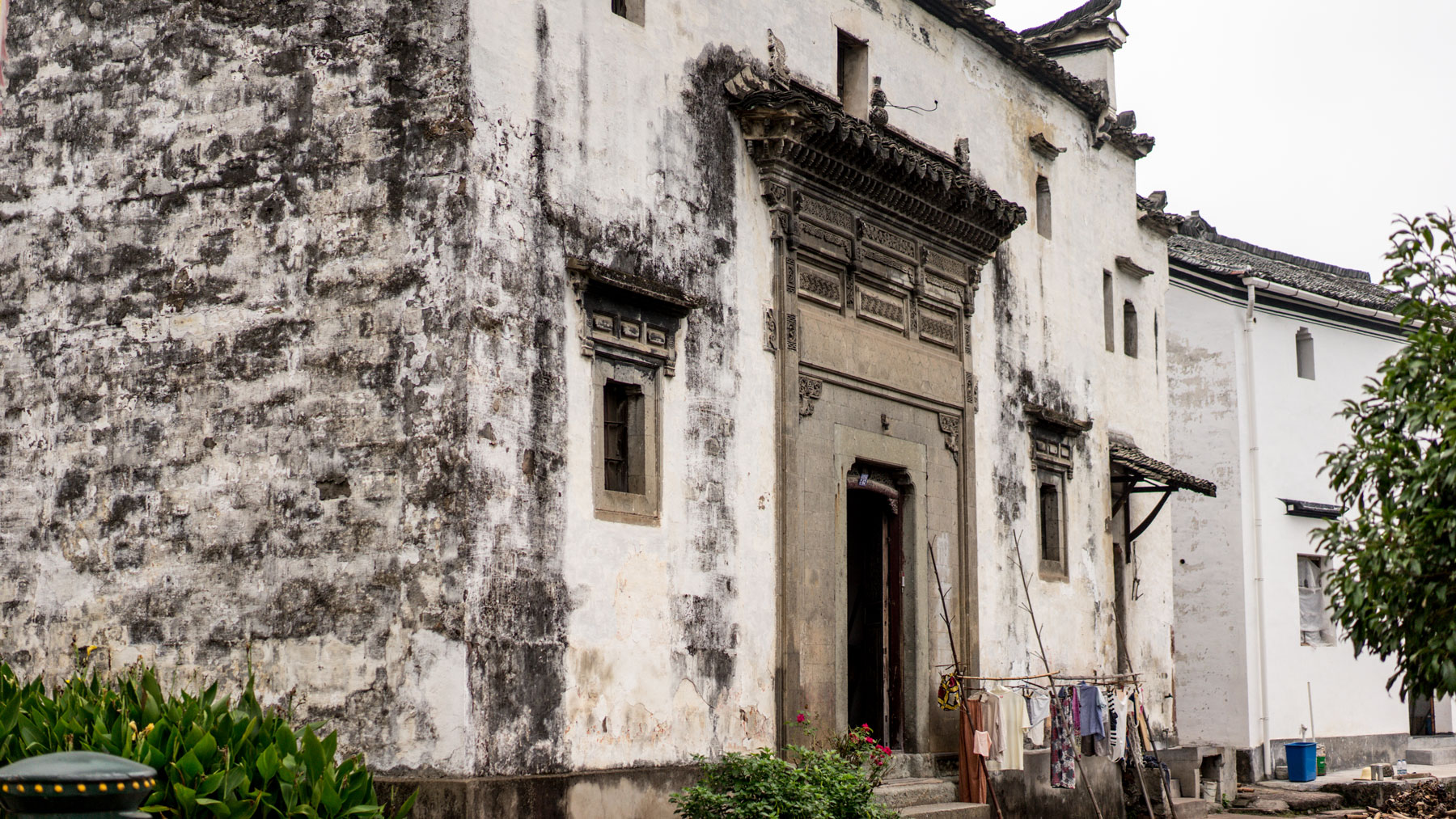 Weathered exterior of a traditional stone and plaster building with an ornate carved doorway and laundry hanging outside, warm earthy tones